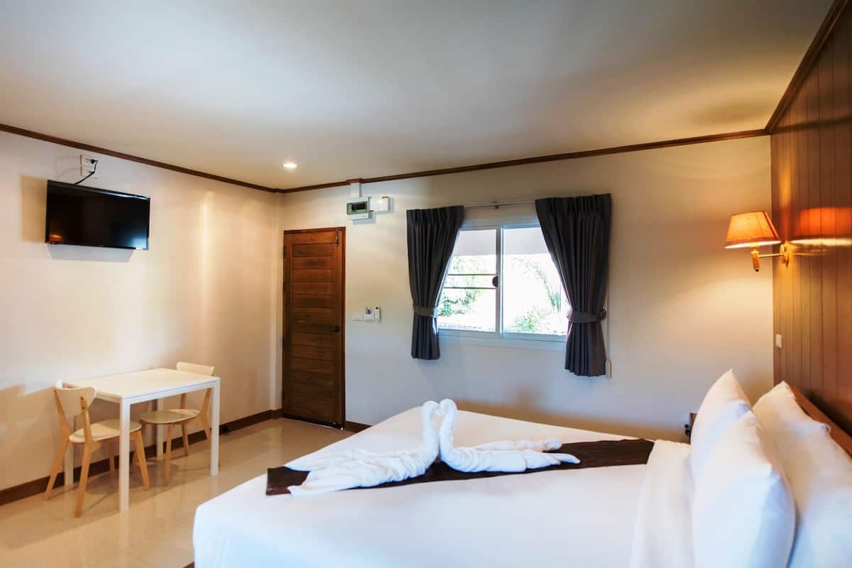 Quarto de hotel com cama, escrivaninha, cadeira, televisão e janela com cortinas.