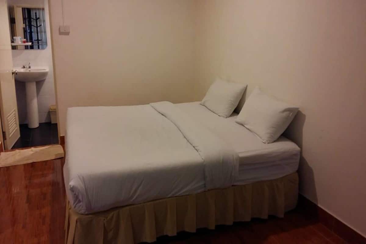 Uma cama de solteiro com saia bege e roupa de cama branca em quarto com piso de madeira e parede branca.