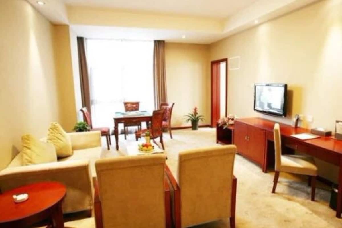 Een hotelkamer met een bank, stoelen, een eettafel, een televisie en een raam.