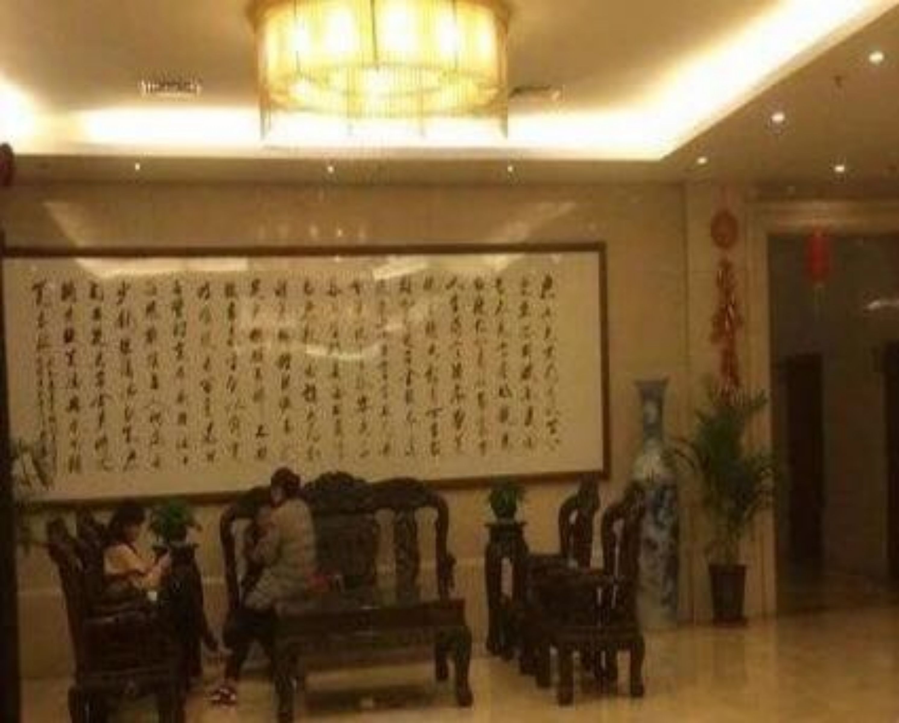 Un hall d’entrée agrémenté d’une grande œuvre calligraphique au mur, de meubles en bois et d’un lustre.