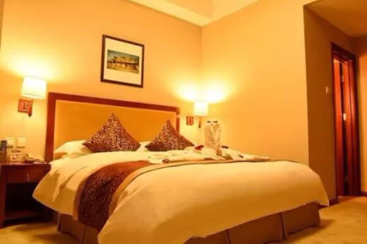 Hotelkamer met een groot bed, twee bedlampen, een ingelijste foto aan de muur en een nachtkastje met een telefoon.