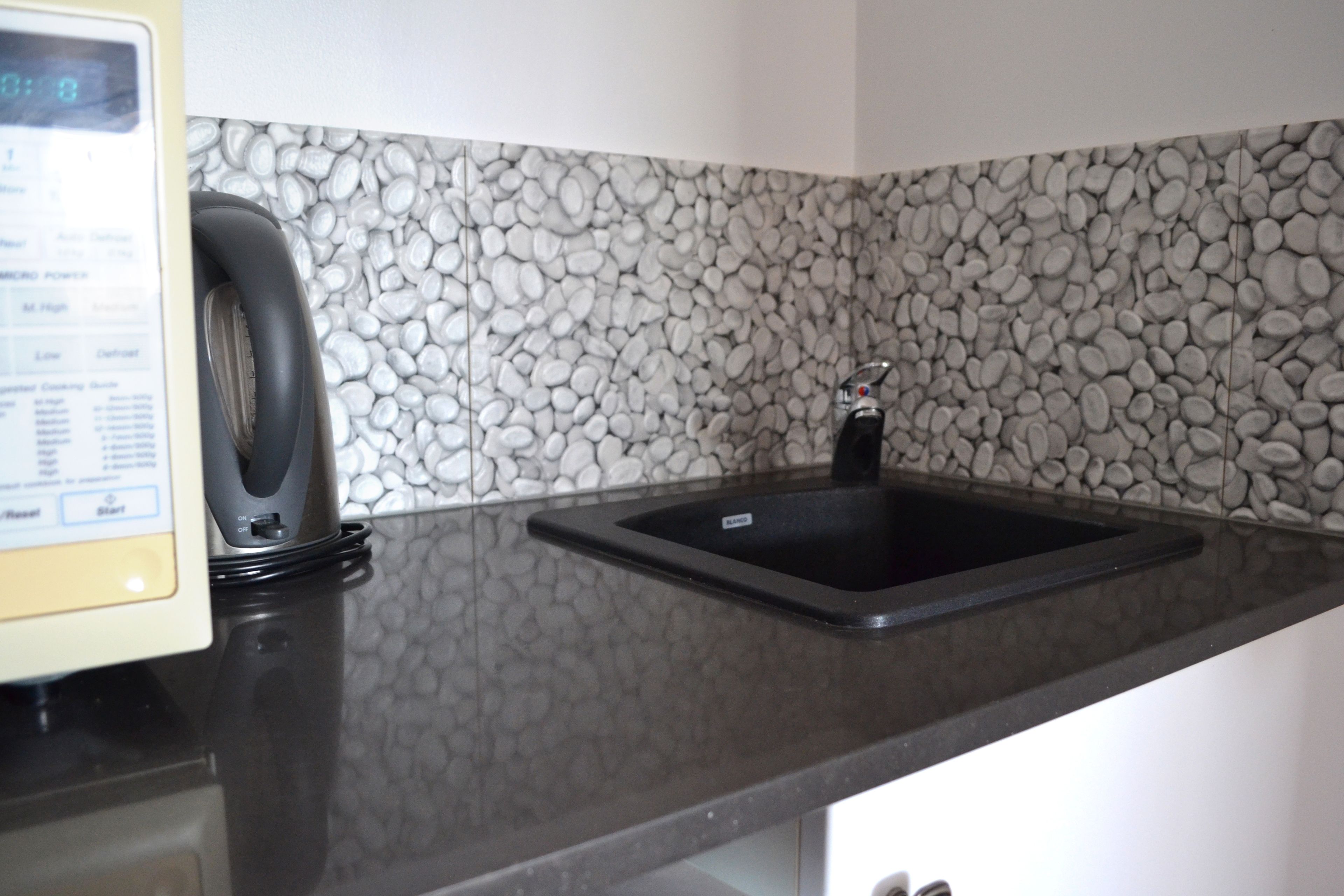 Una cocina con encimera de granito, un lavamanos negro y una cafetera.