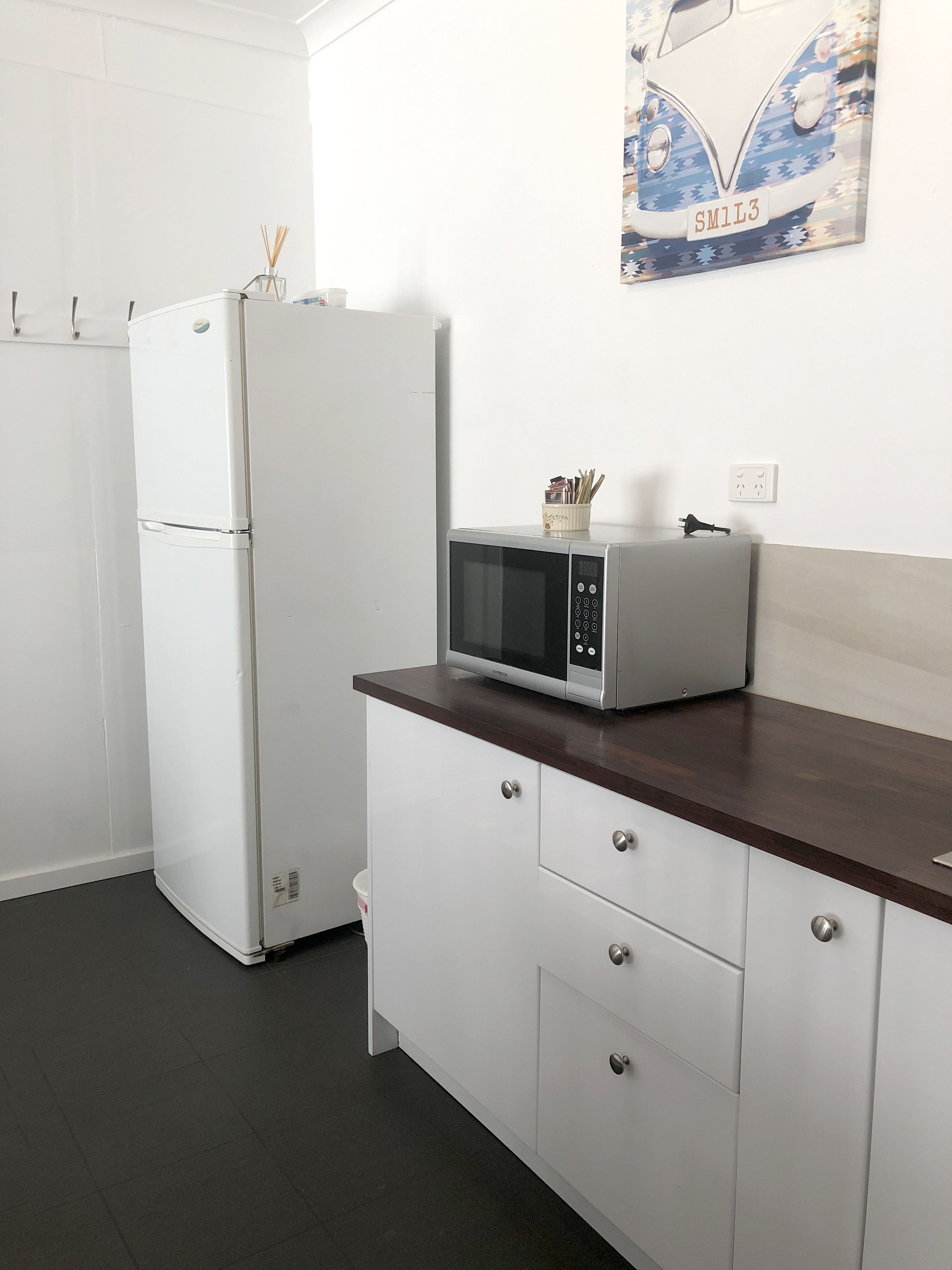 A kitchen with white cabinetry, a microwave on a wooden countertop, and a refrigerator.