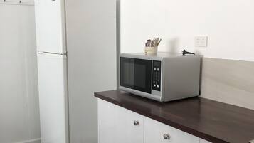 A kitchen with white cabinetry, a microwave on a wooden countertop, and a refrigerator.