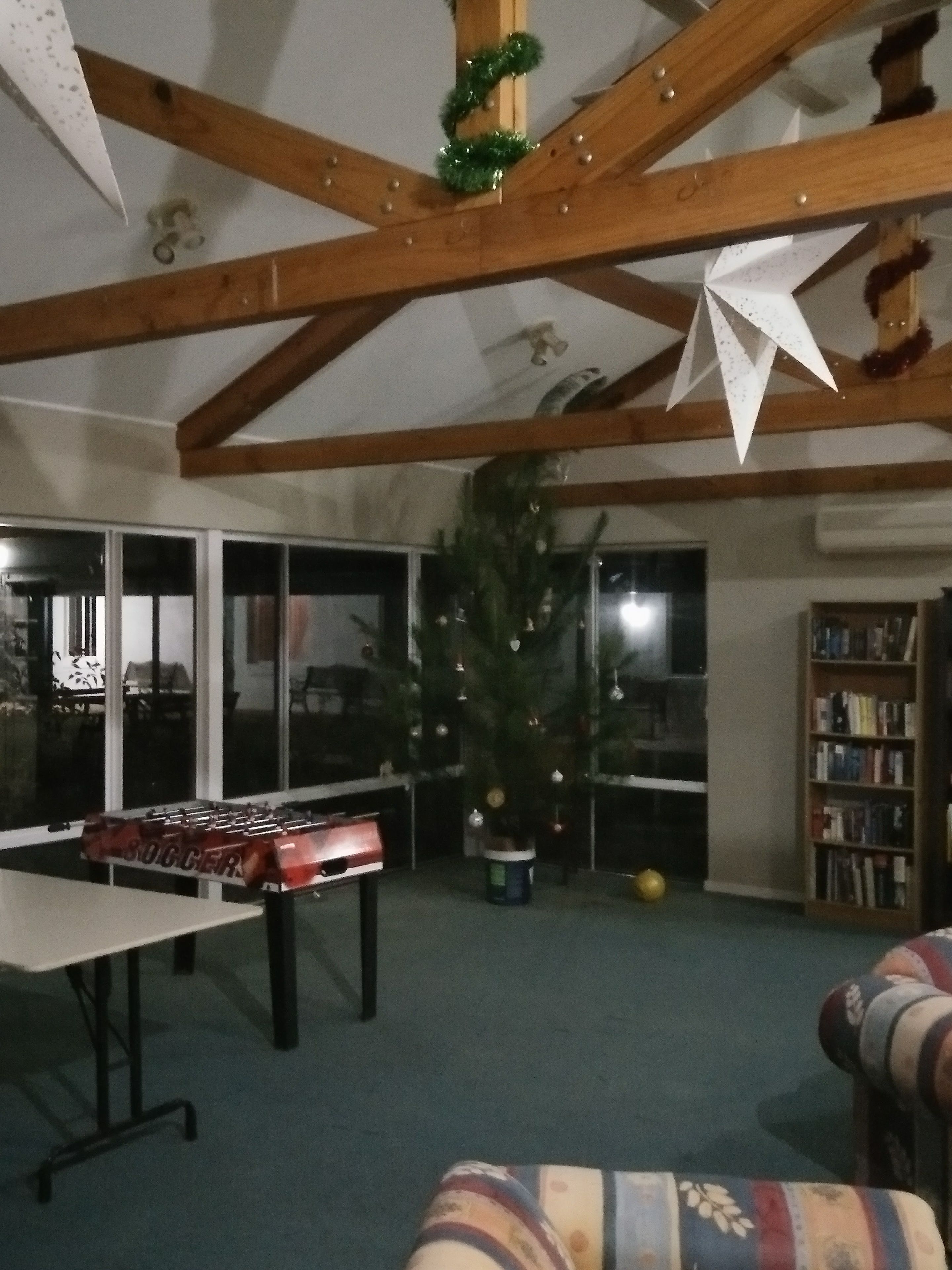 A room with a wooden ceiling, a foosball table, a Christmas tree, and a bookshelf.