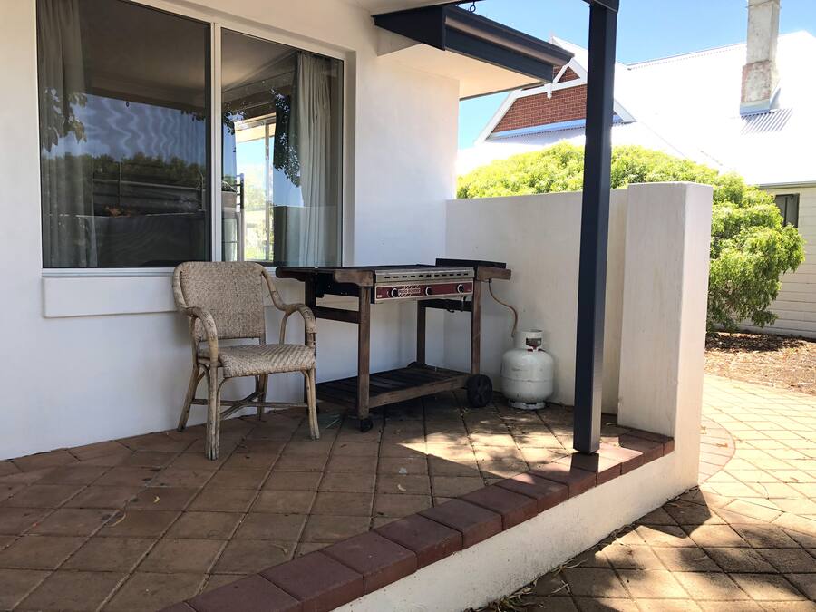 Un patio con una silla de mimbre, una mesita y un tanque de propano.