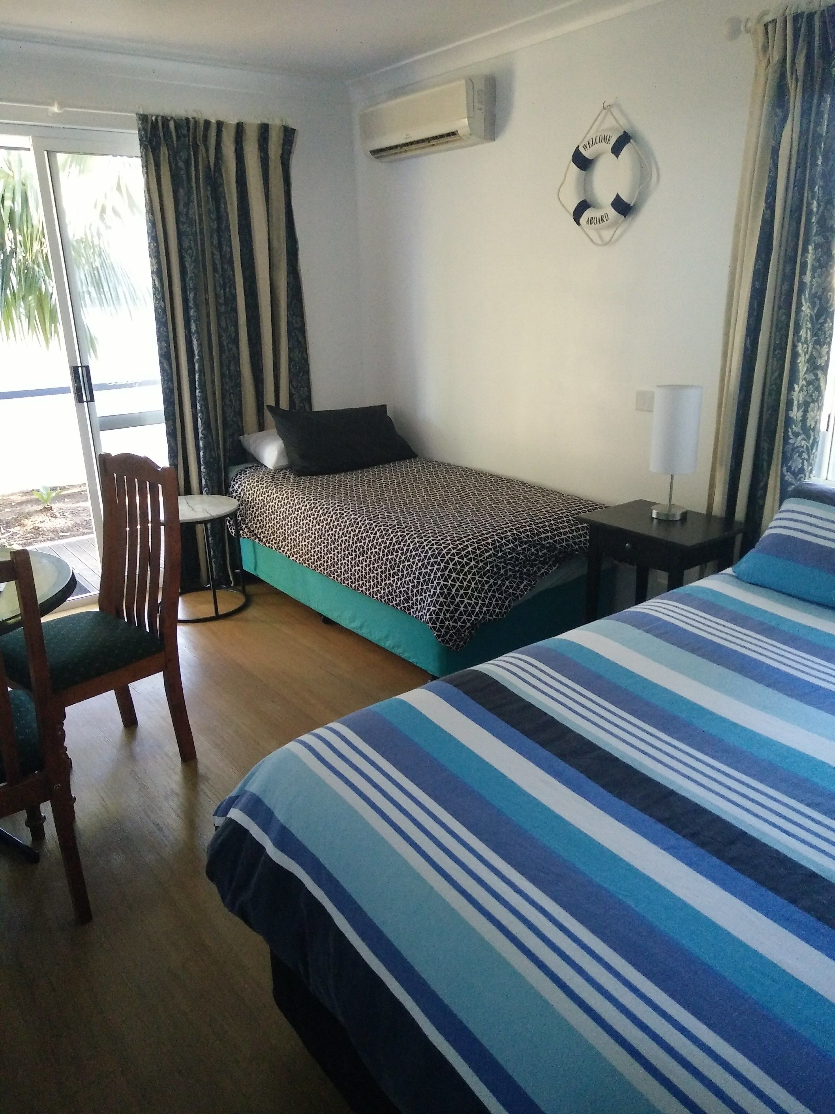 Une chambre d’hôtel équipée d’un lit, d’une chaise, d’une petite table, d’un appareil de climatisation et d’un panneau d’accueil.