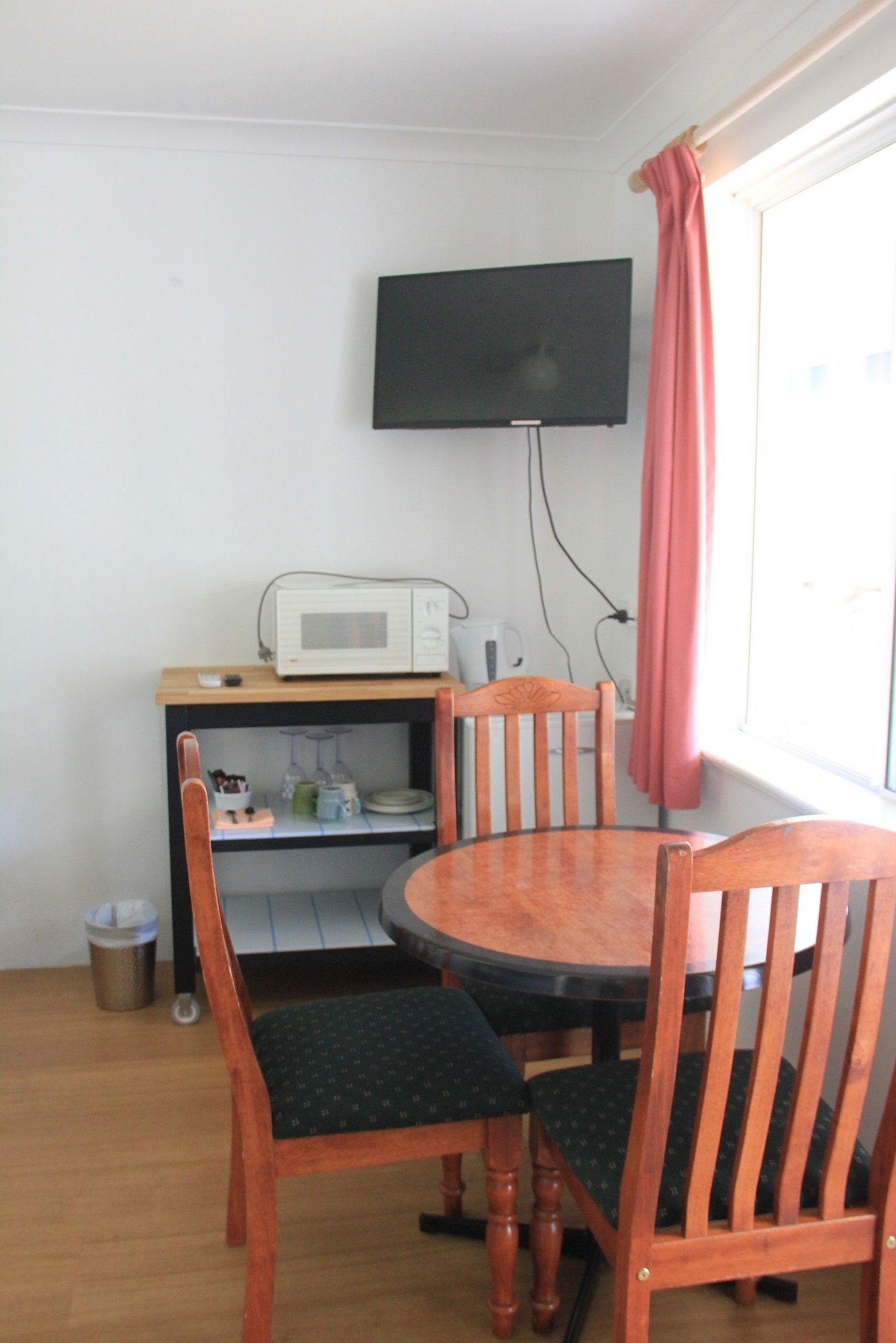 A small dining area with a wooden table and chairs, a microwave, and a TV mounted on the wall.