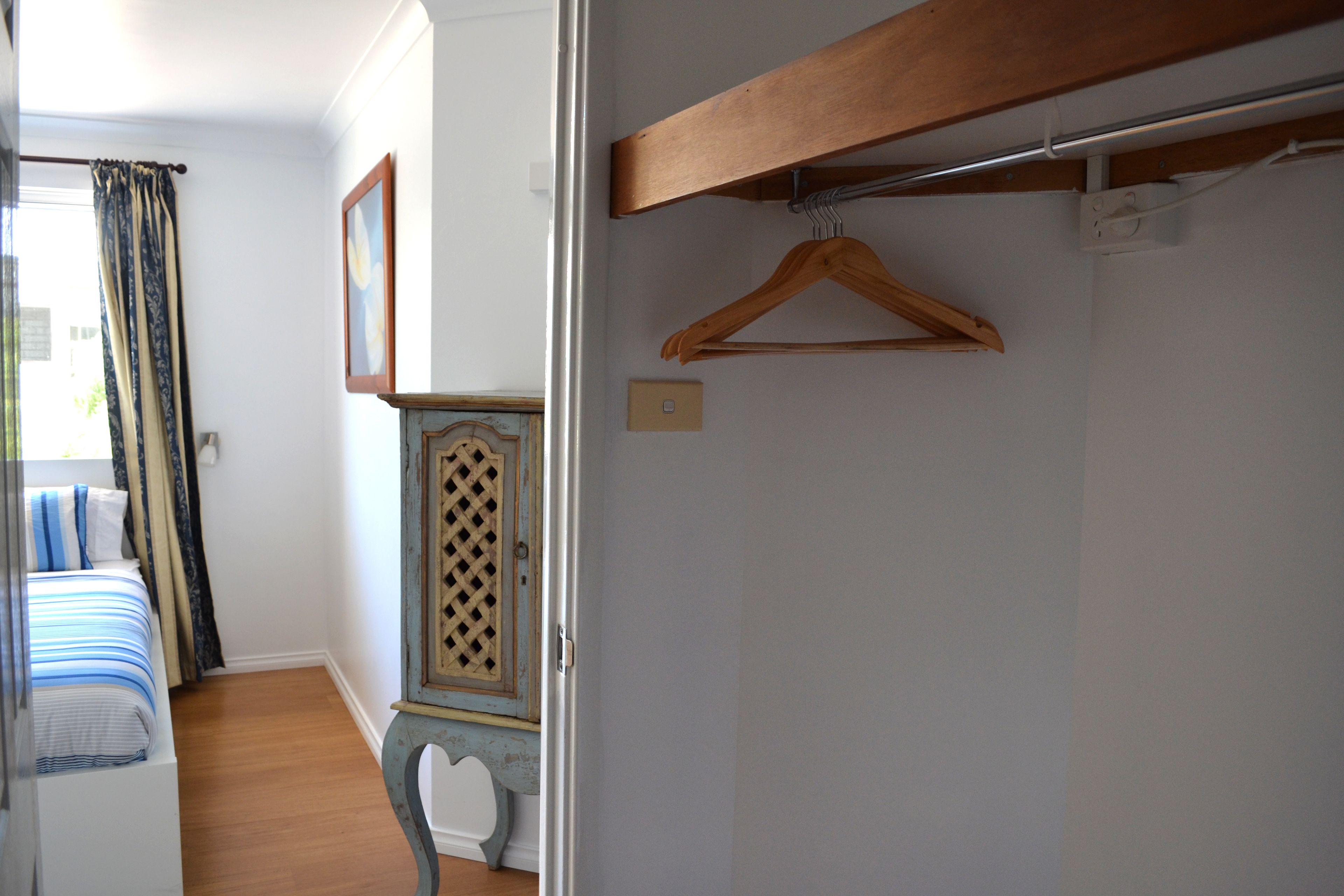 Un dormitorio con una cama, un aparador de madera, un perchero colgante de madera y un interruptor de luz en la pared.