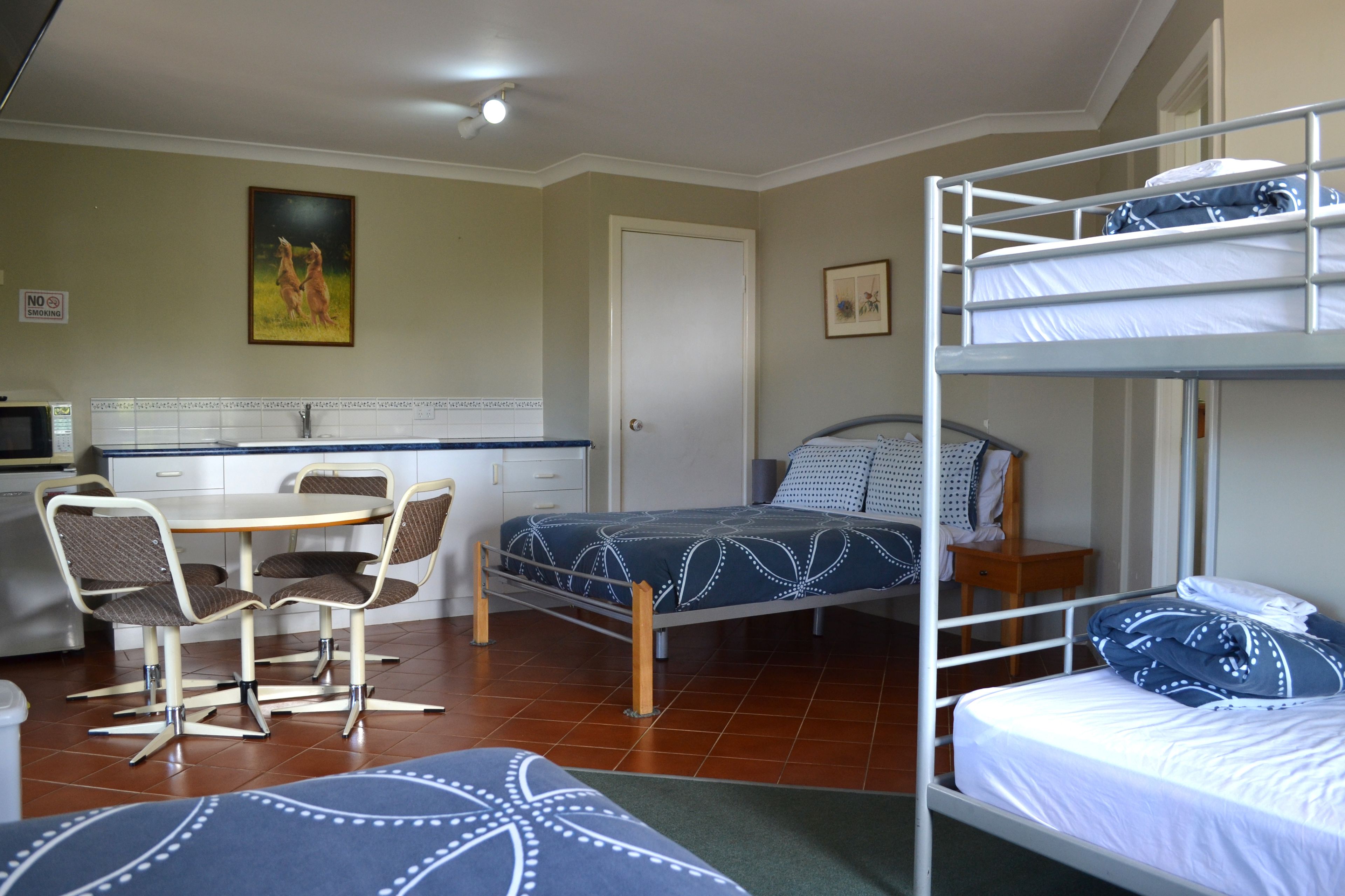 Una habitación compacta con literas, una mesa de comedor con sillas, una zona de cocina y una puerta.