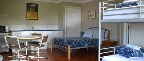 A compact room with bunk beds, a dining table with chairs, a kitchen area, and a door.