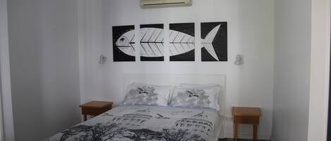 A bedroom with a bed, two nightstands, a wall-mounted air conditioner, and three wall art pieces depicting fish.