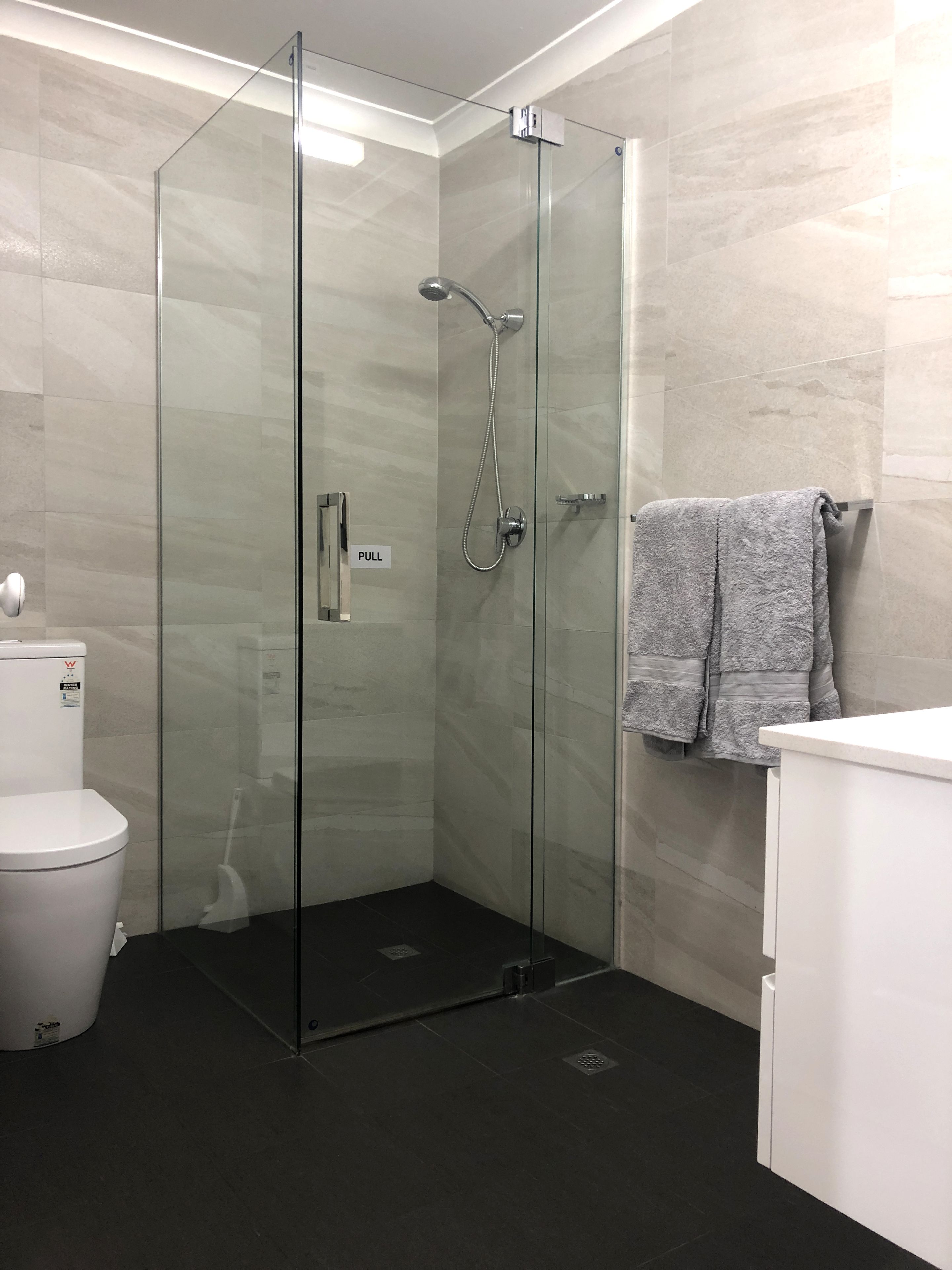 Un baño moderno con ducha envuelta en vidrio, inodoro y lavamanos con toallero.