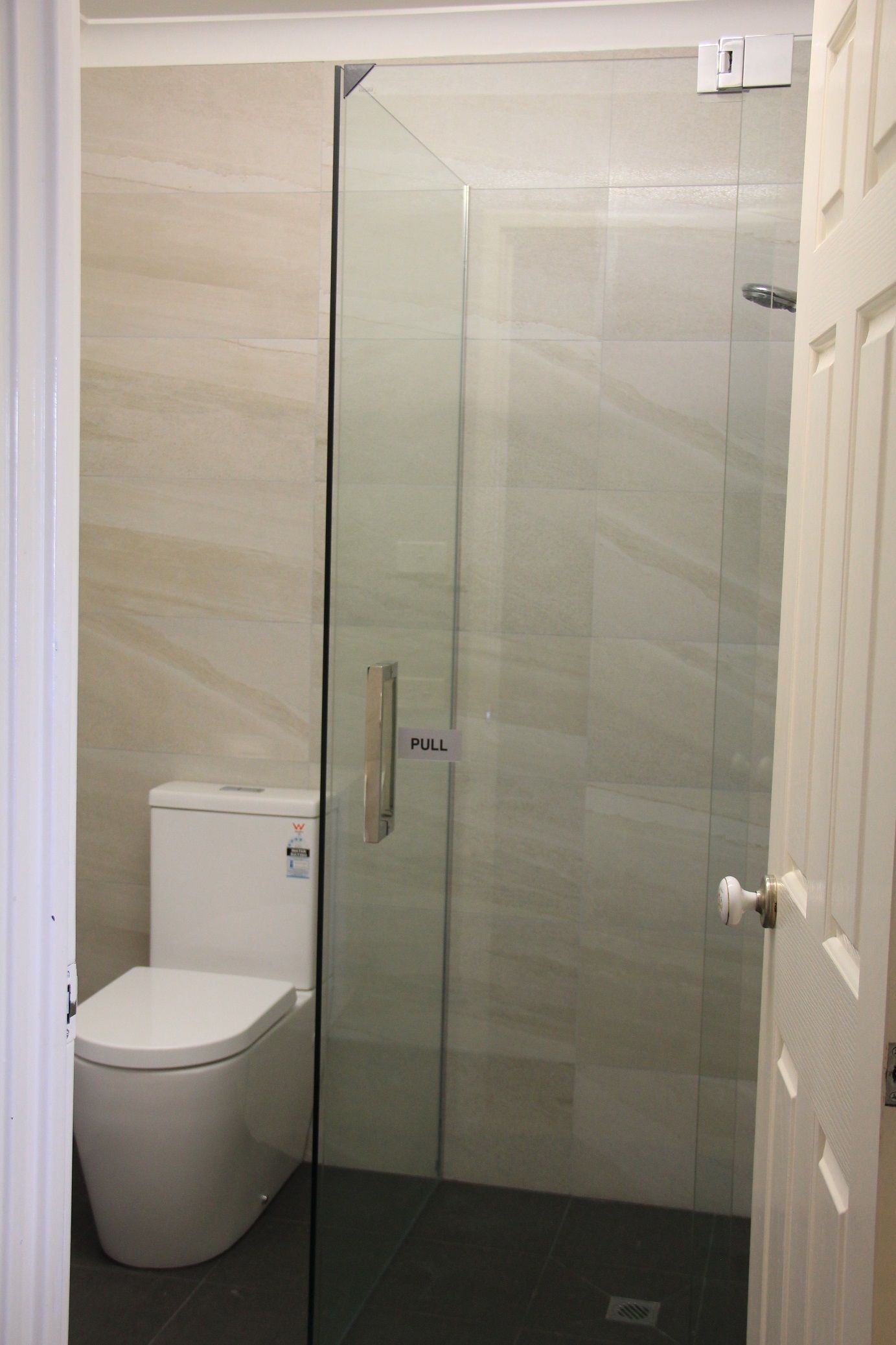 Un baño con cabina de ducha de vidrio, inodoro blanco y un tirador en la puerta de cristal.