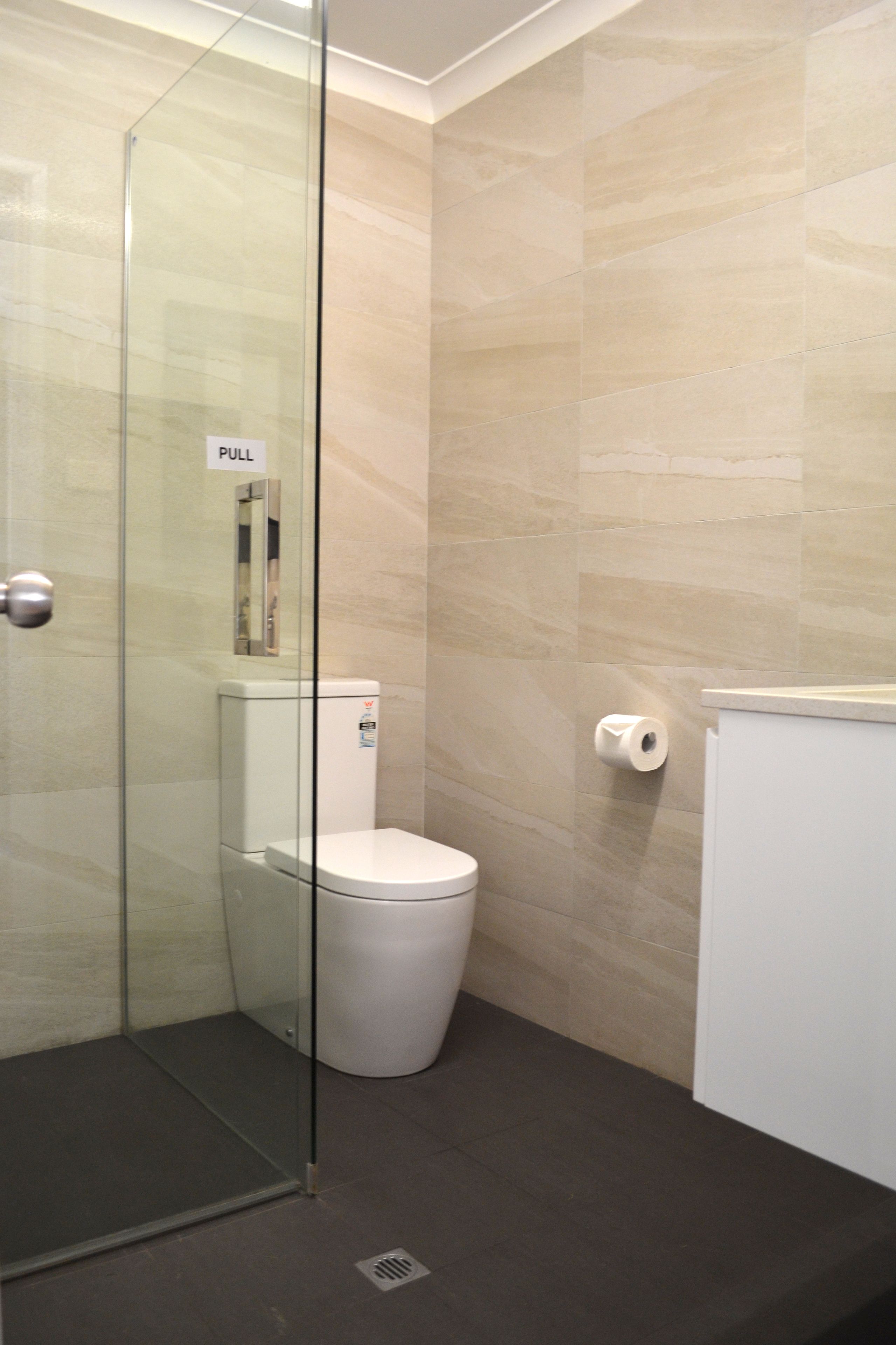 A modern bathroom with a glass shower enclosure, a toilet, and a paper towel dispenser.