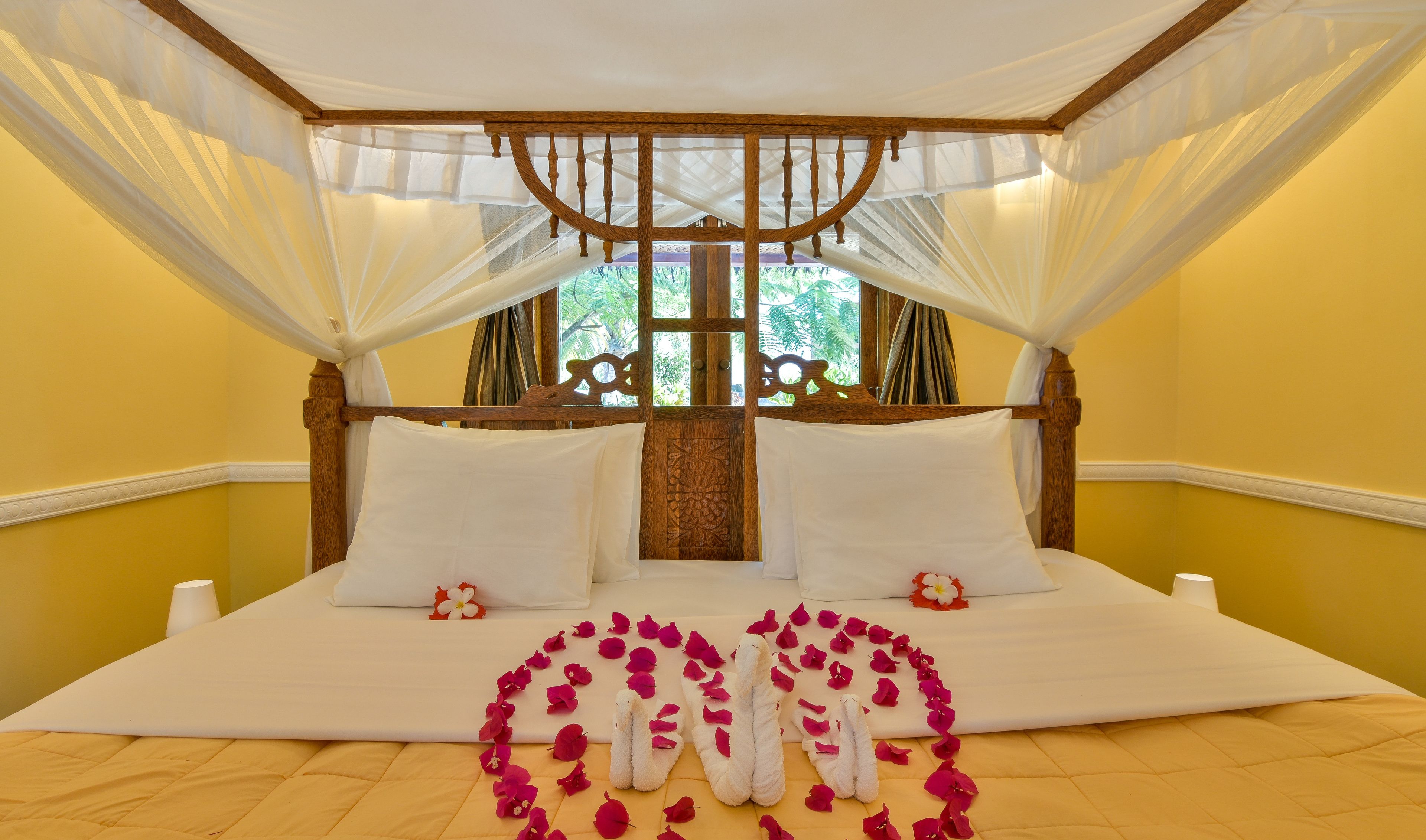A bed with a canopy, white linens, and a floral arrangement on the bed.