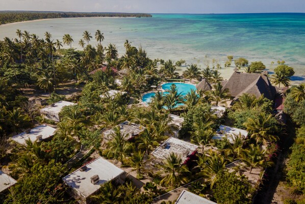 Un complejo turístico con varias edificaciones tipo bungalow, una piscina central y vista a la playa.