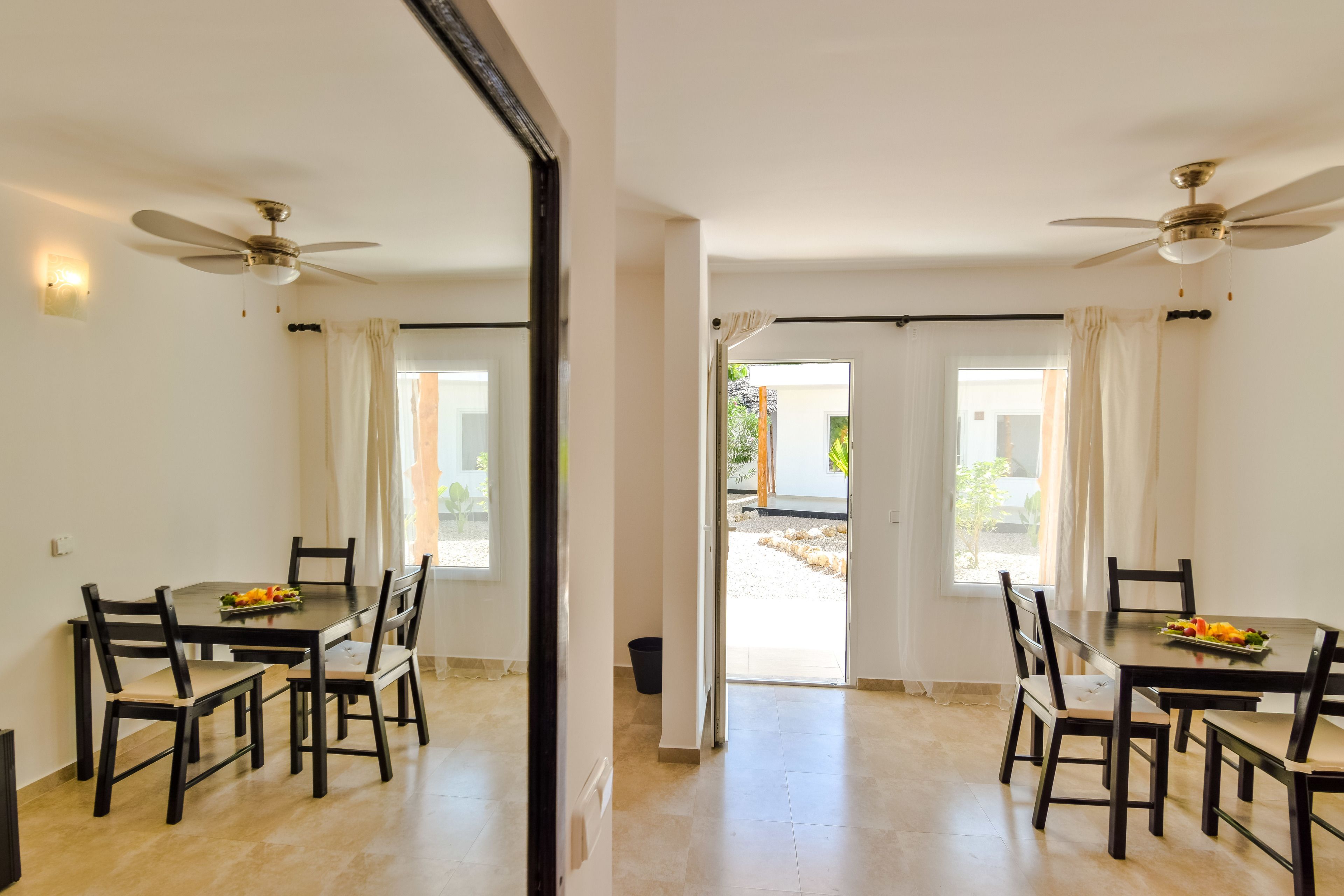 A dining area with a table and chairs, a ceiling fan, and a view through an open door to an outdoor space.