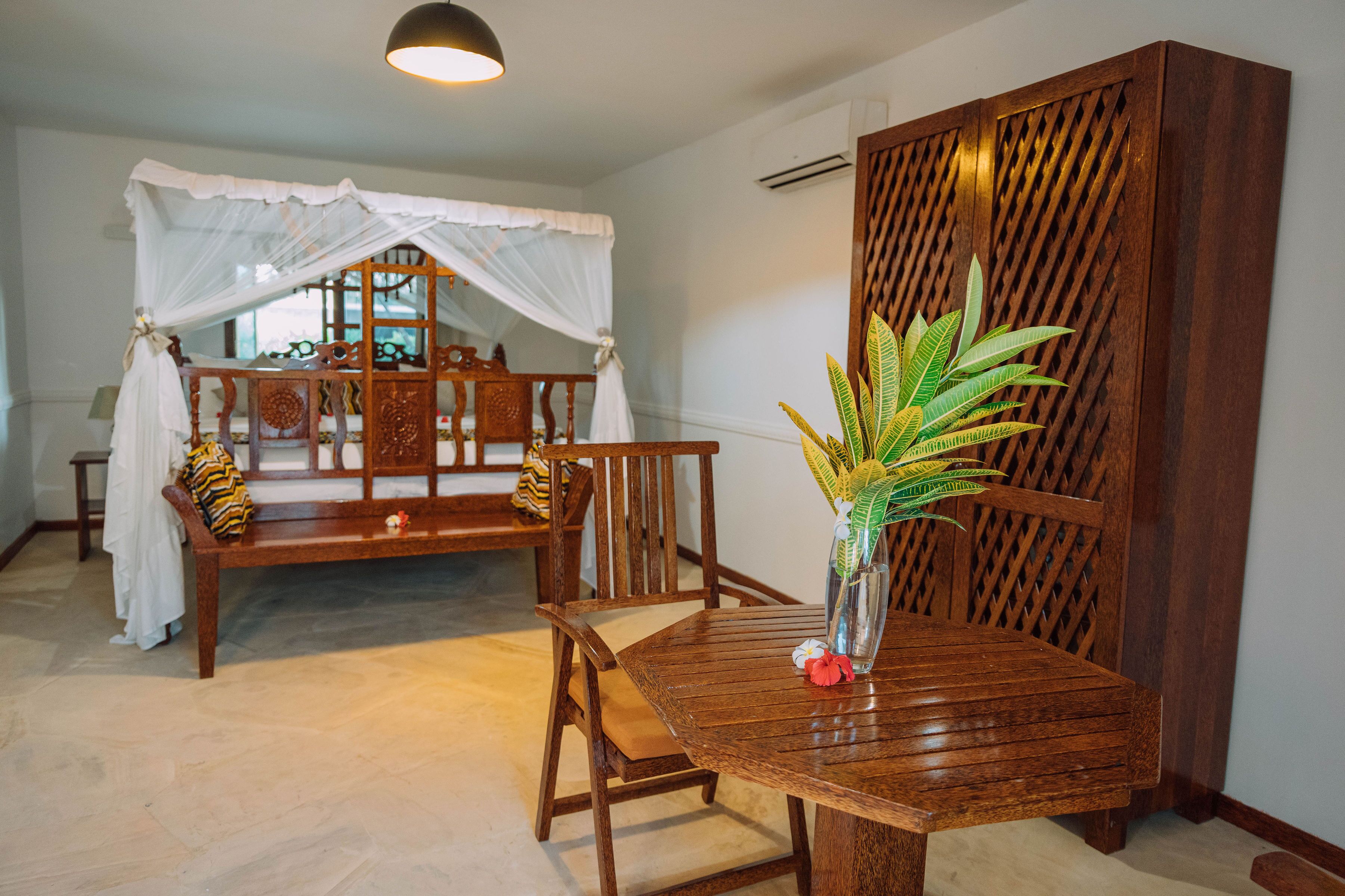 A room with a wooden bed, a wooden table with a vase, and a wooden partition.