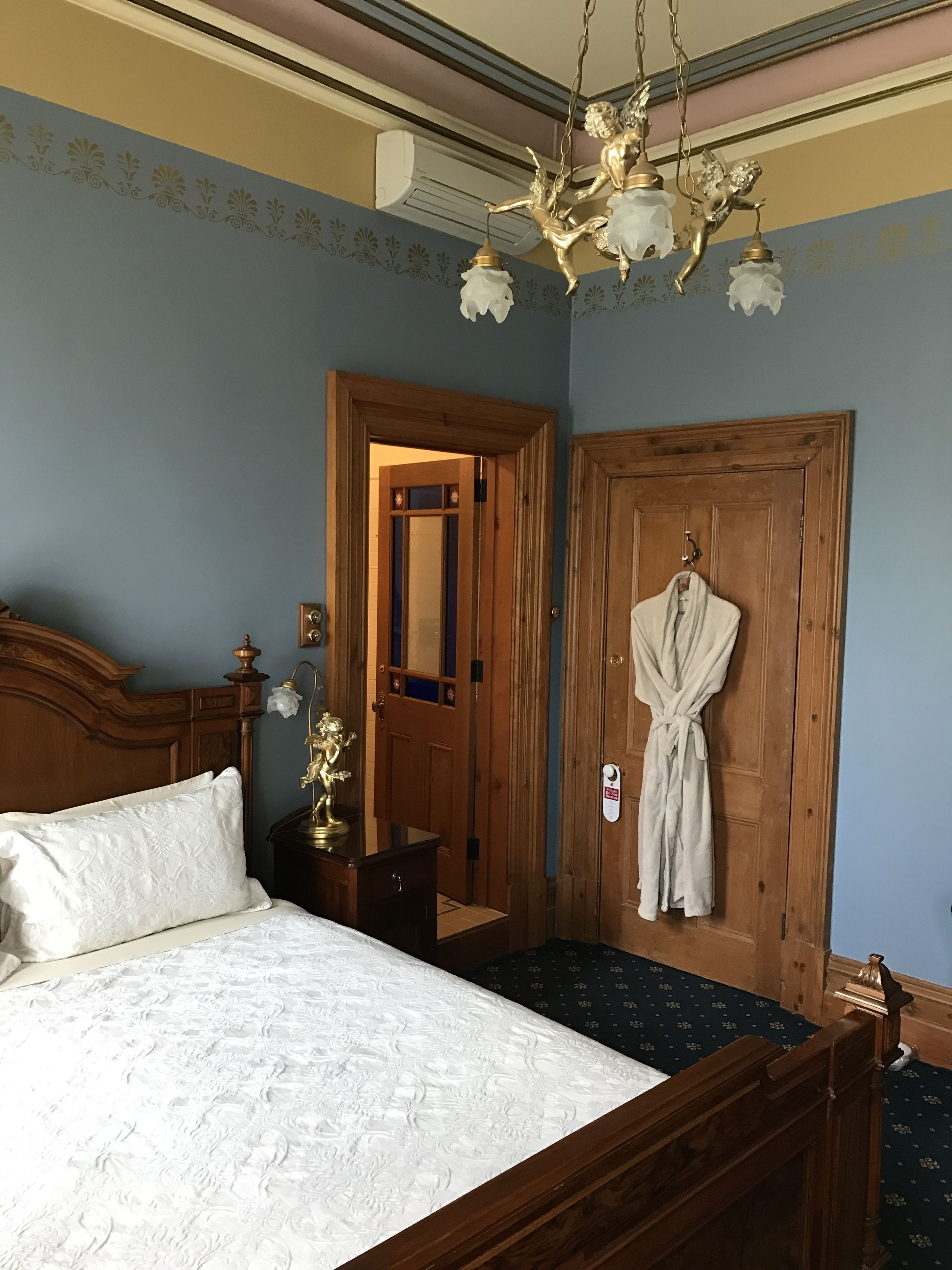 Un dormitorio con una cama grande, cabecera de madera, una lámpara de araña, una bata colgada en una puerta y un espejo.
