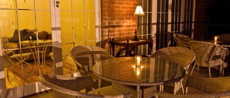 An outdoor patio with wicker furniture and a glass table, surrounded by brick walls and arched windows.
