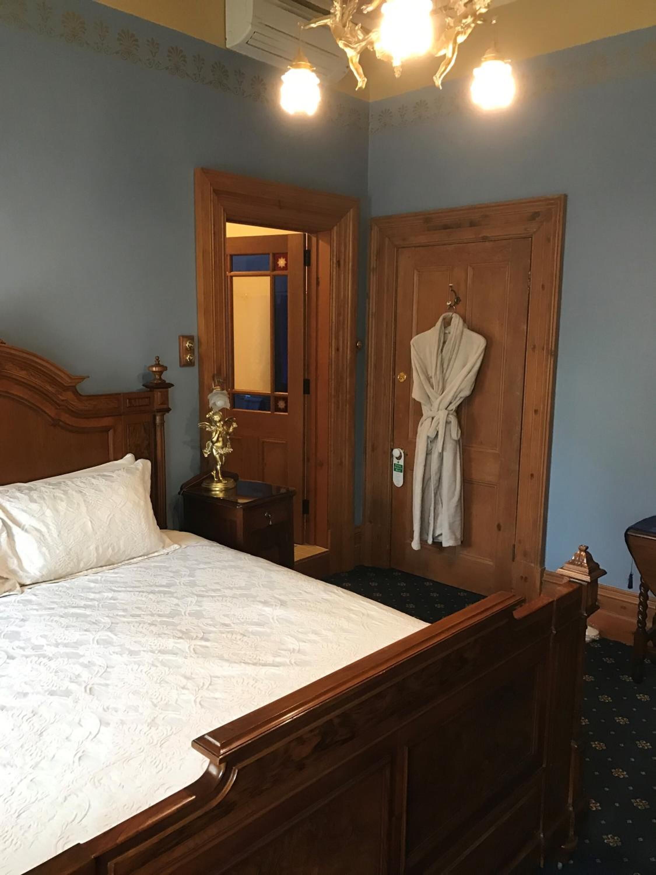 A bedroom with a large bed, wooden headboard, a robe hanging on the door, and a chandelier.