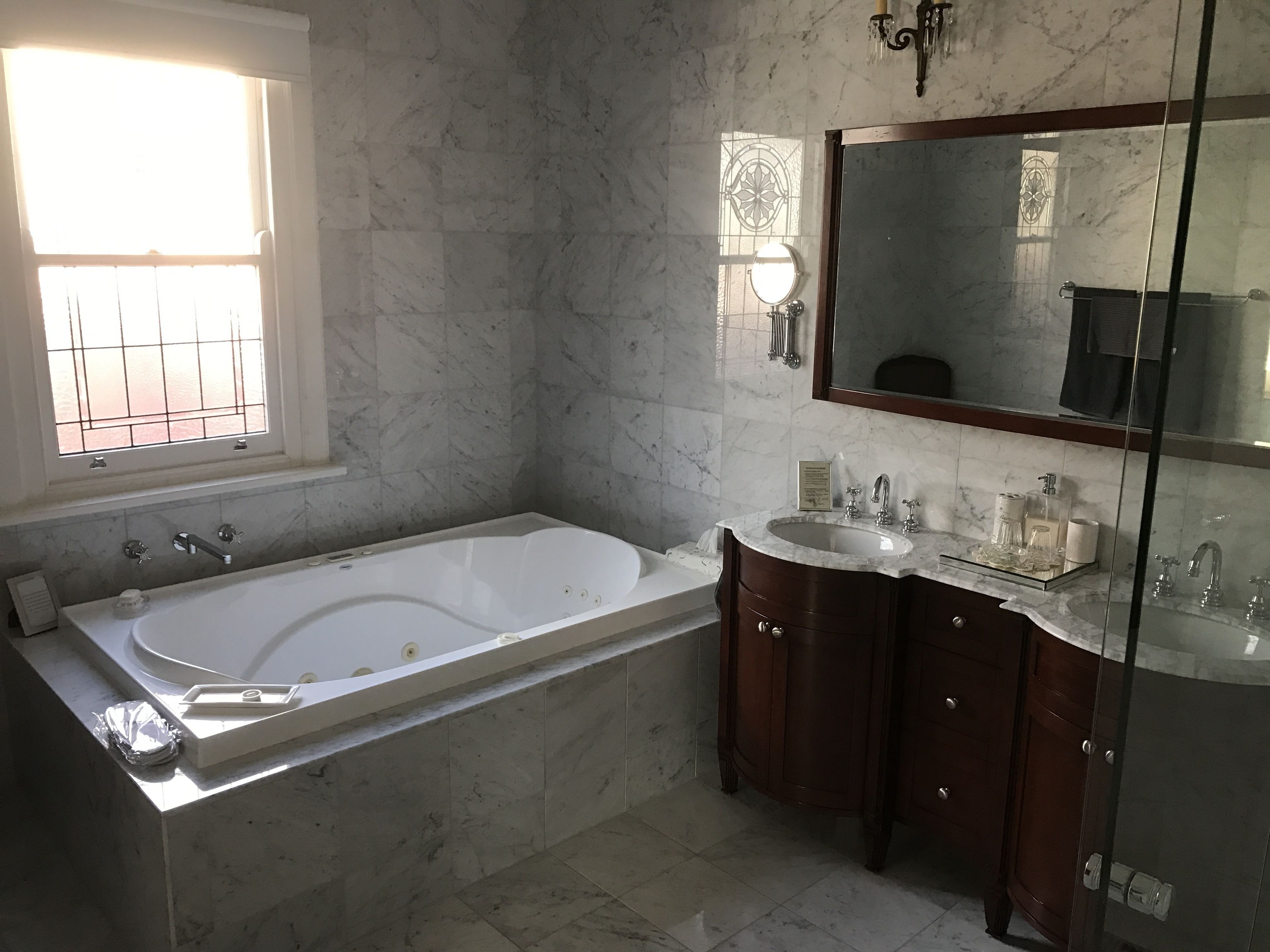 A bathroom with a large bathtub, a vanity with a mirror, and a window with bars.