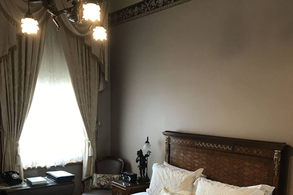A neatly made bed with a patterned bedspread, a wooden headboard, and a chandelier above.