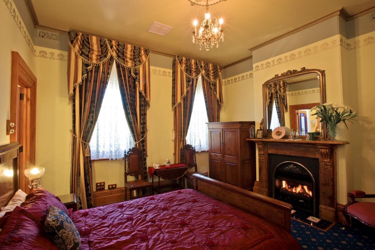 A traditional room with a large bed, a fireplace, and a mirror above it.