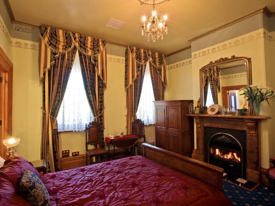 Una habitación tradicional con una cama grande, una chimenea y un espejo encima.