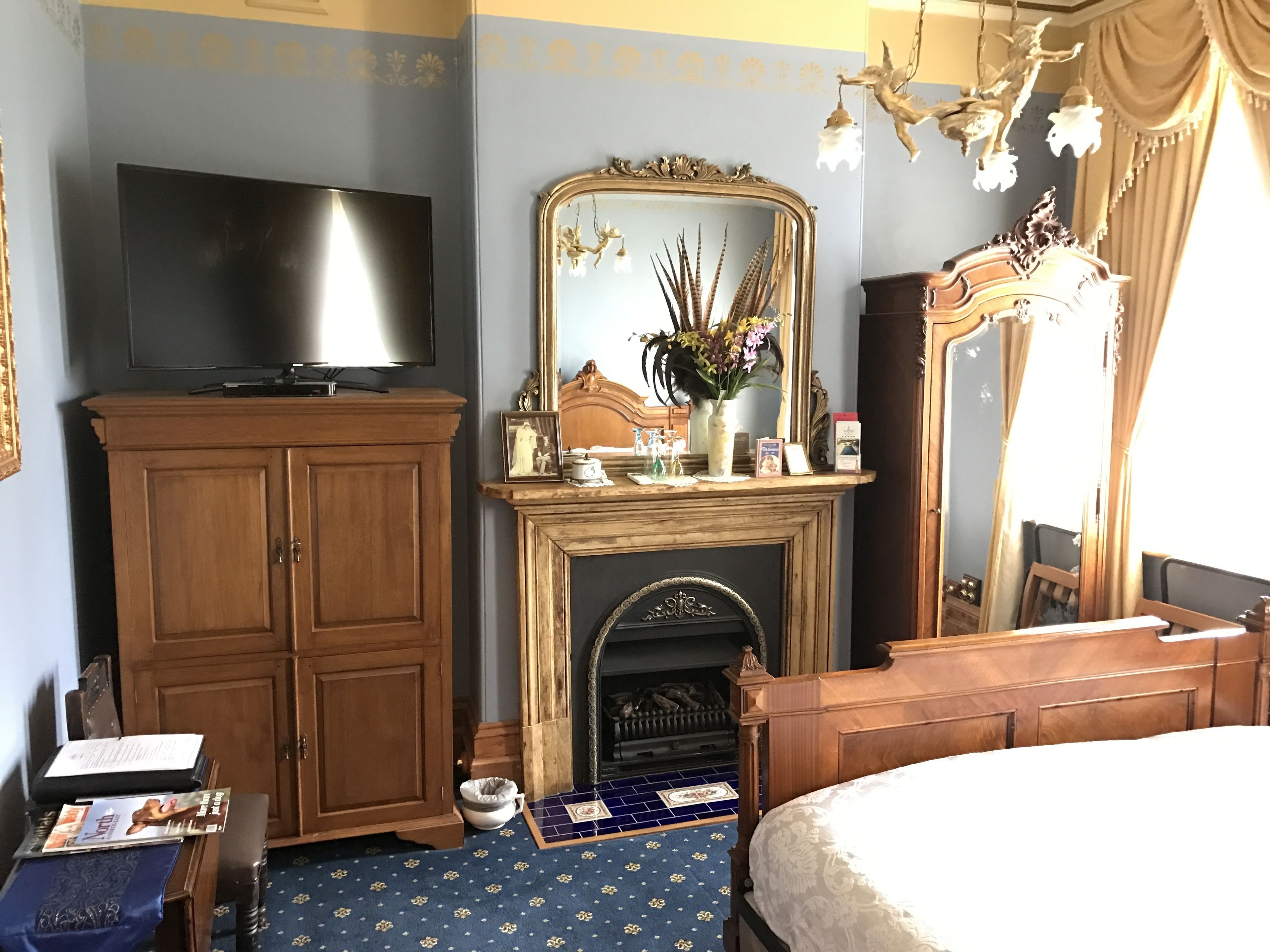 A bedroom with a wooden wardrobe, a television, a fireplace, and a large mirror.