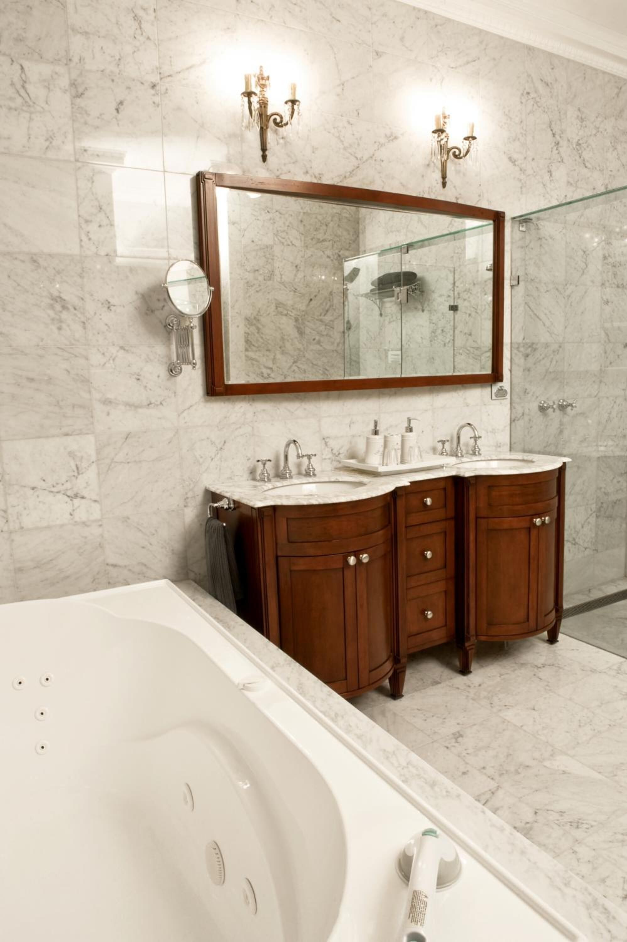 Un bagno con un grande specchio, due lavabi, una vasca e pareti in marmo.