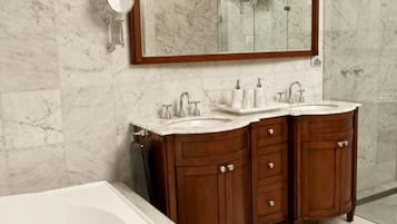Un bagno con un grande specchio, due lavabi, una vasca e pareti in marmo.