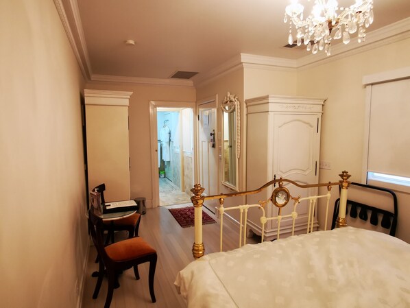 A bedroom with a bed, a desk, and a chair. There is a mirror and a chandelier.