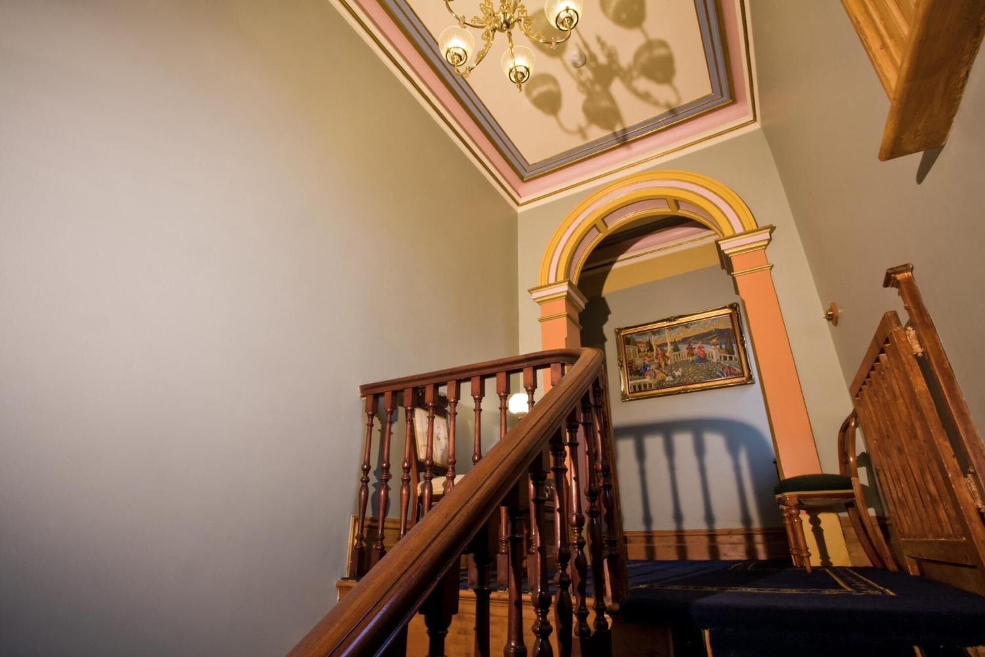 A staircase with wooden balusters and a handrail, leading to a landing with a framed picture and a chair.