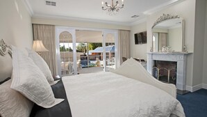 A spacious bedroom with a large bed, a fireplace, and a balcony with outdoor furniture. - Freeman On Ford (Beechworth)