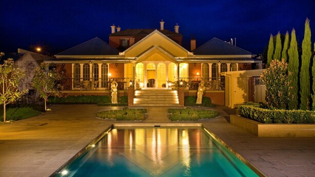 A large, well-lit building with a pool in front, surrounded by landscaped gardens and tall trees. - Freeman On Ford (Beechworth)