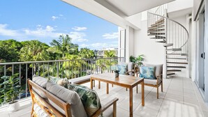 Ein Balkon mit Holztisch und -stühlen, einer Couch und einer Wendeltreppe.