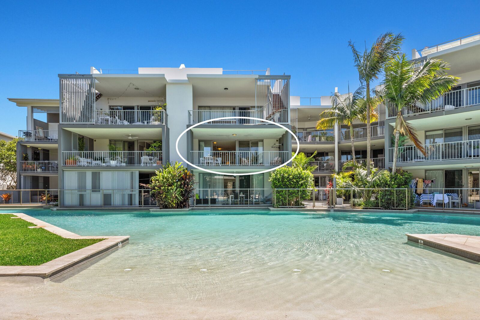 A modern hotel with a pool, multiple balconies, and lush landscaping.