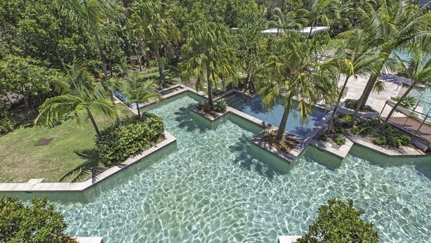Ein Poolbereich mit mehreren Schwimmbecken, umgeben von üppiger Vegetation und Palmen.