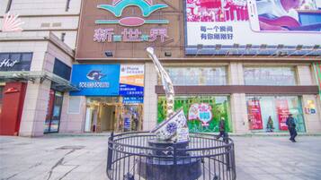 A shopping mall with a central fountain, various storefronts, and a large digital advertisement.