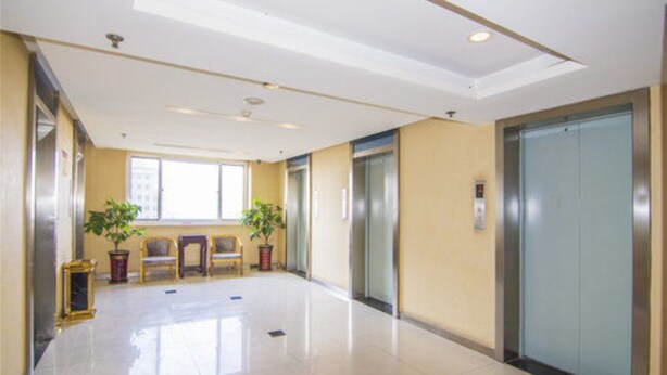 A clean, well-lit hallway with two elevators, potted plants, and a seating area with chairs. - Golden Tree Business Hotel (Xi'an)