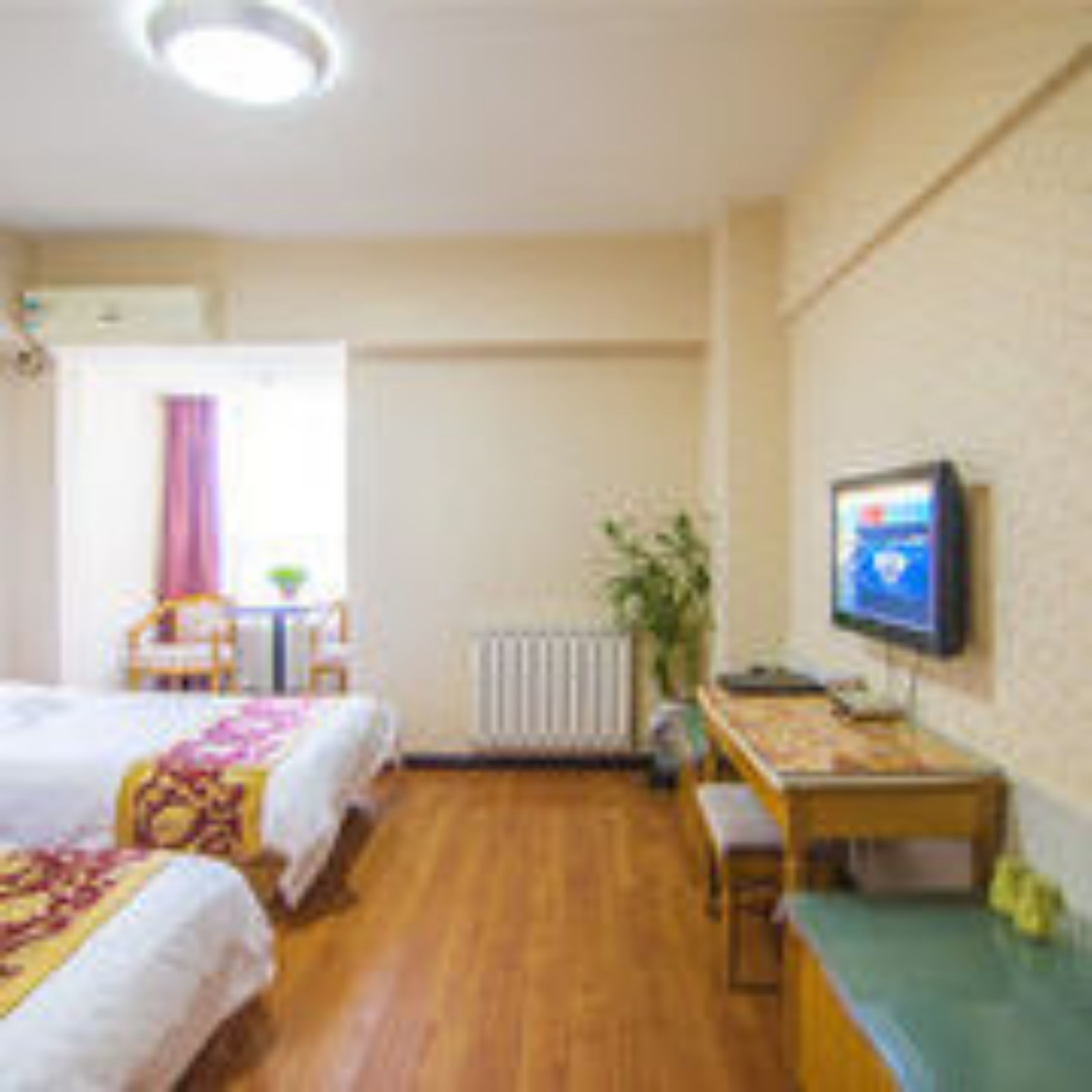 A hotel room with two beds, a desk, a chair, a radiator, a television, and a window with curtains.