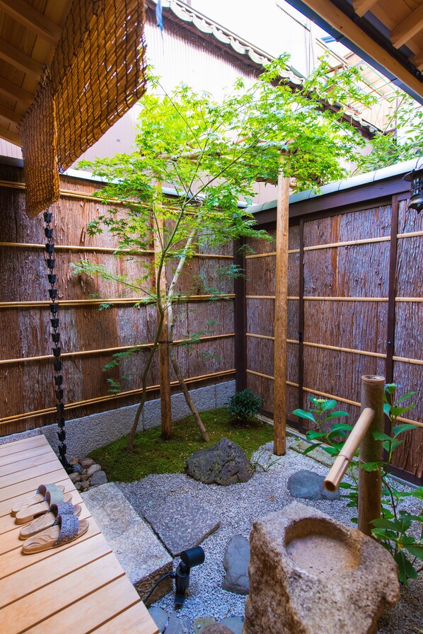 A traditional Japanese garden with a wooden deck, bamboo fence, and a small pond.