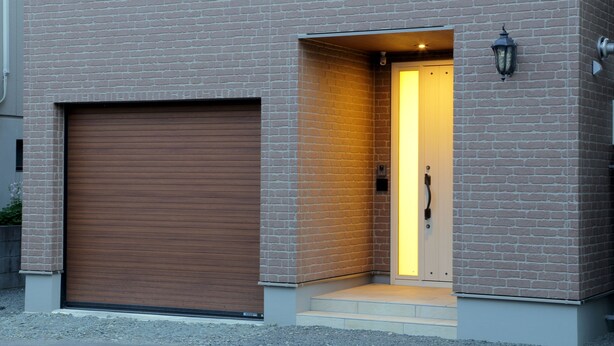 A modern building with a brick facade, a large garage door, and a well-lit entrance with steps leading up to a door. - OCHO Guest House - Hostel (Sapporo)
