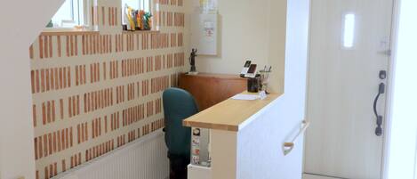 A small office space with a desk, chair, and a radiator. There is a door with a handle and a window with blinds.
