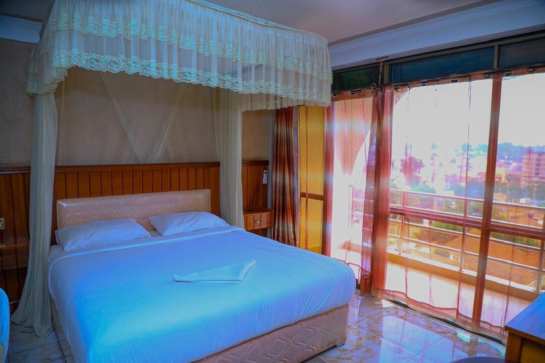 Une chambre d’hôtel avec un grand lit, un baldaquin, une vue sur la ville par la fenêtre et un balcon avec des rideaux.