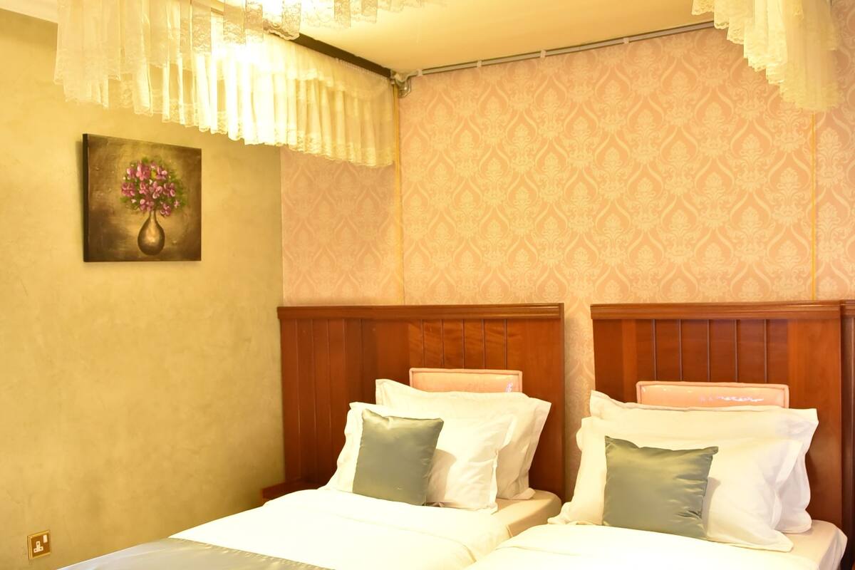 A double room with two beds, a large window, and a painting on the wall.