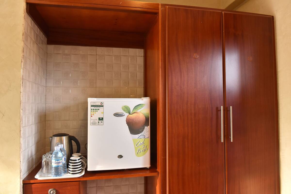 A kitchen area with a refrigerator, a kettle, and water bottles on a countertop.