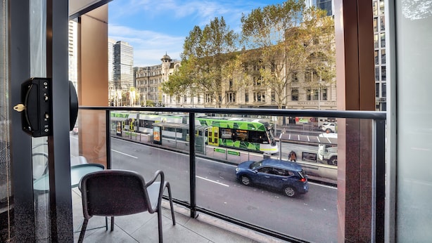 A view from a hotel room with a large window overlooking a street with a green bus and a car. - All on Flinders (Melbourne)